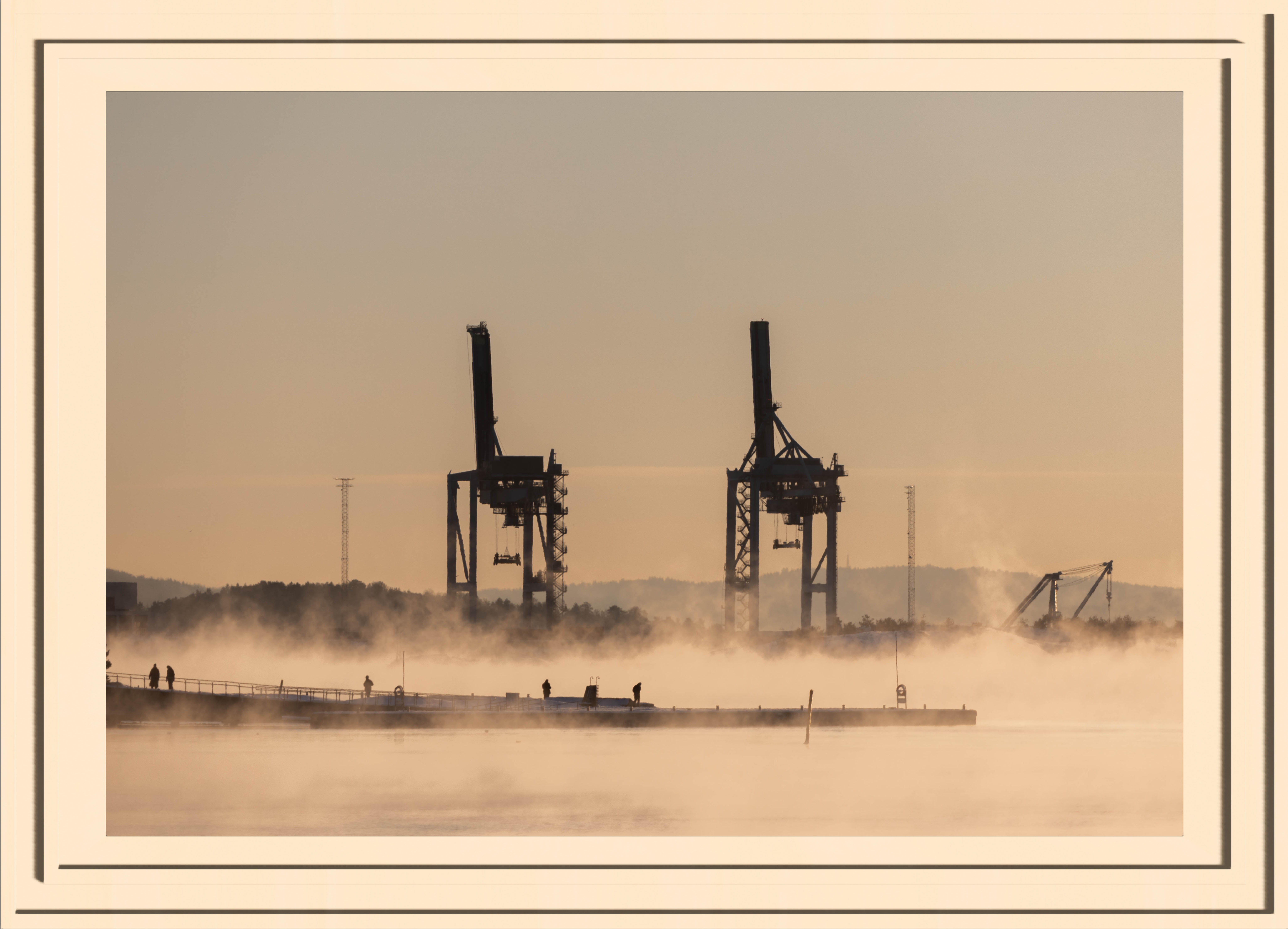industrial port in the background with small silhouettes of people walking on a harbour