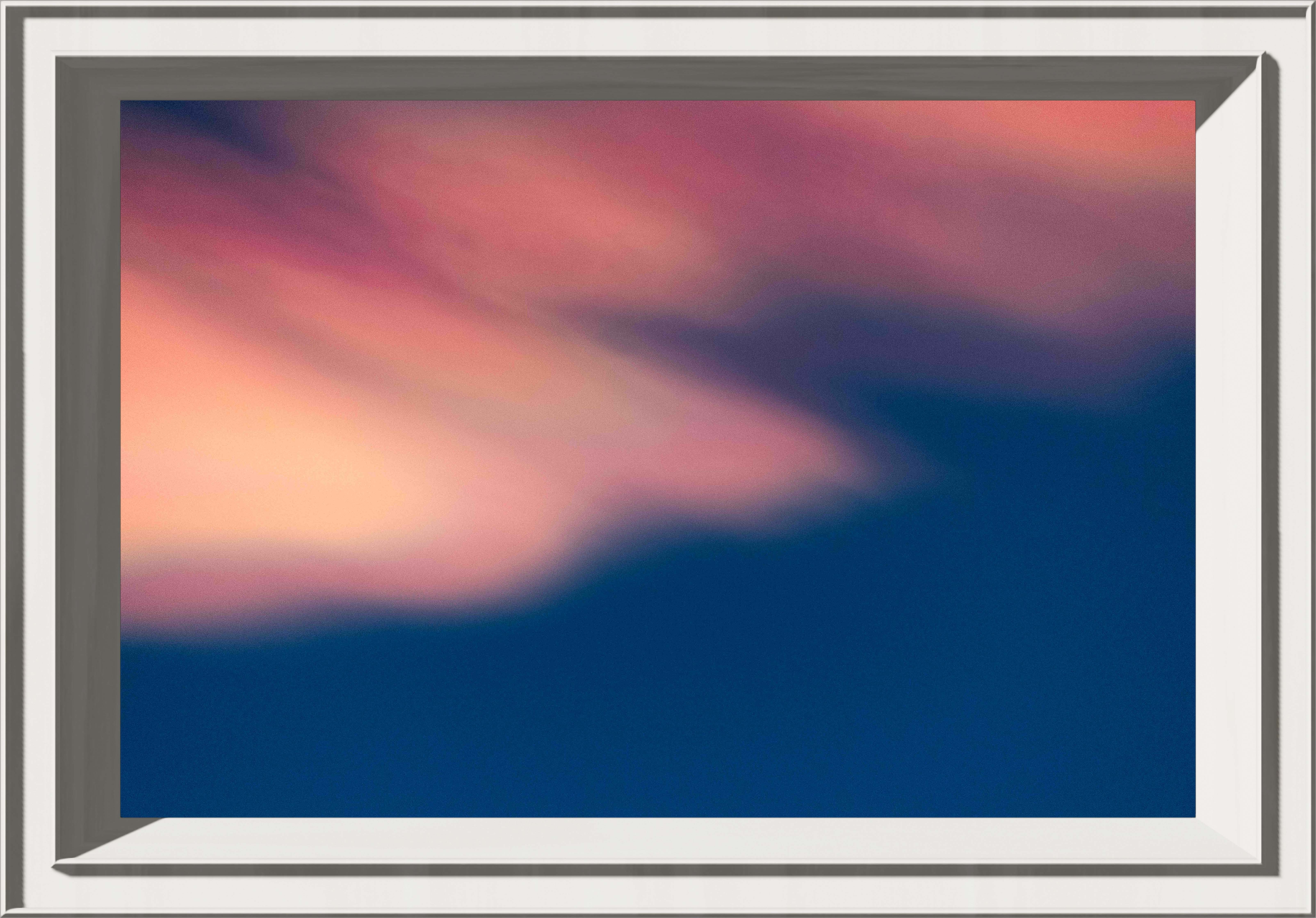 Rainbow clouds lit by the setting sun making them pink in a dark blue sky