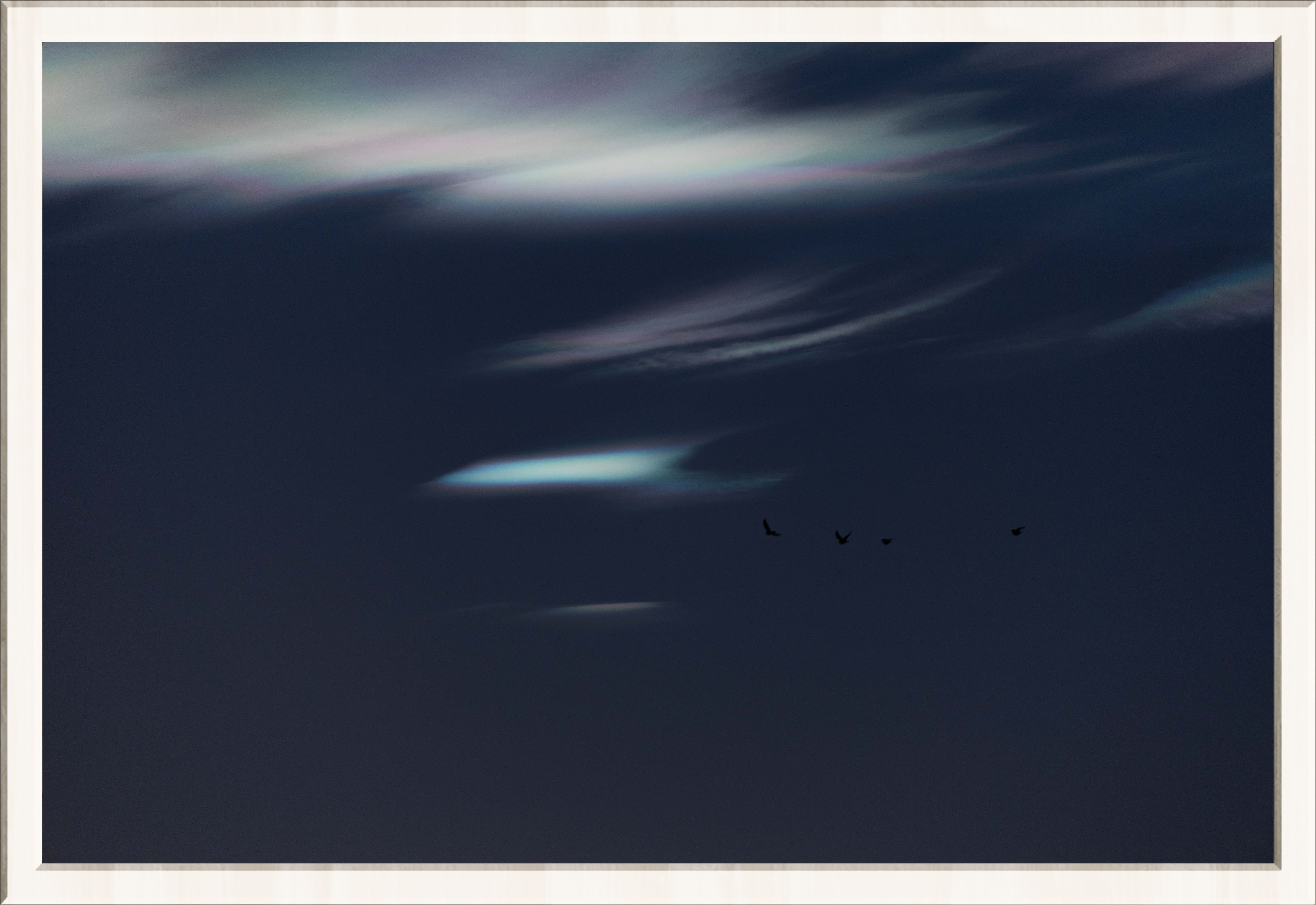 Iridescent Clouds in a dark sky that are silky and diffused with 4 small birds flying, in a thin white frame