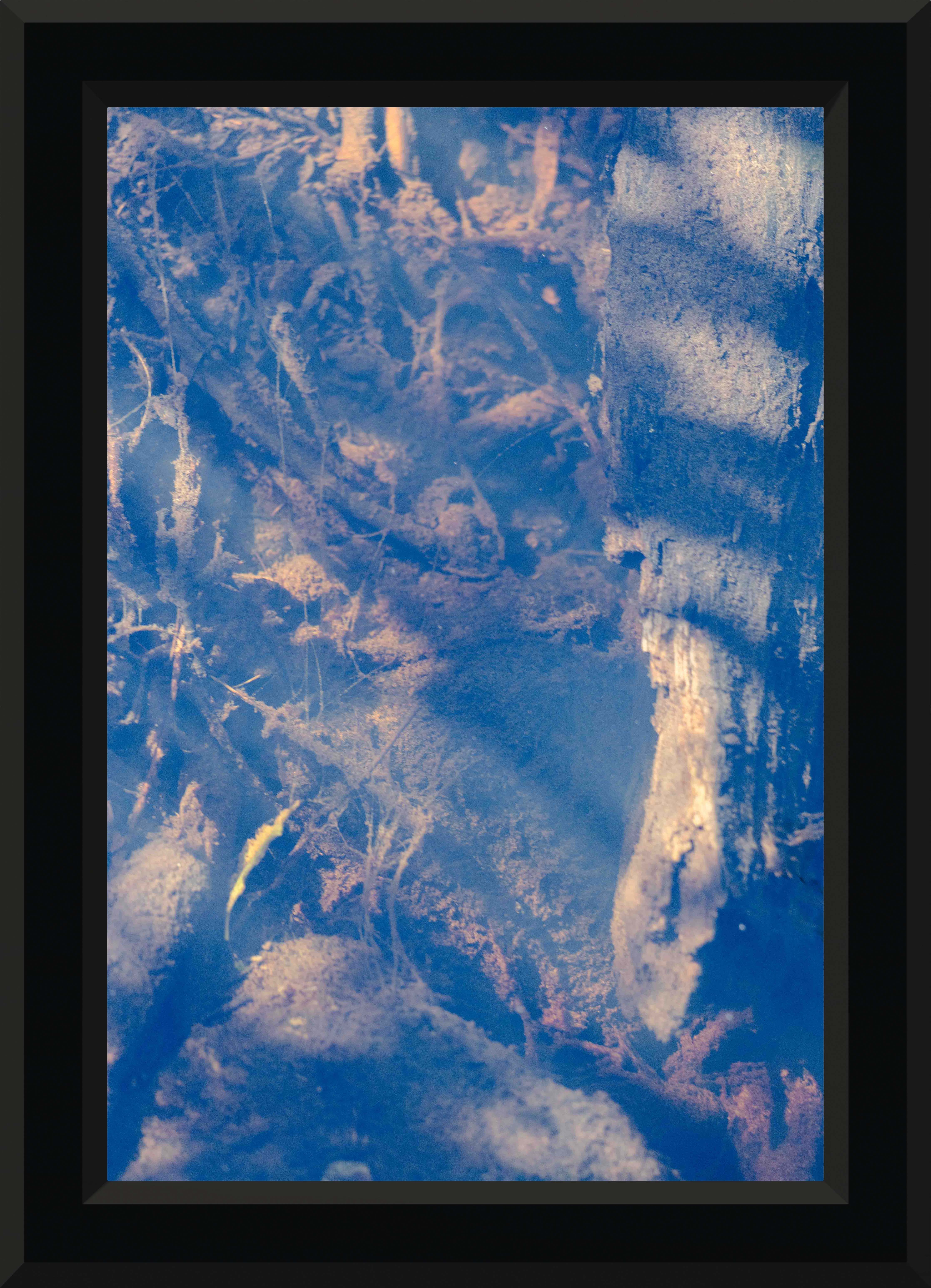 A riverbed seen from the top that has a blue reflection from the sky, framed in a thick black frame.