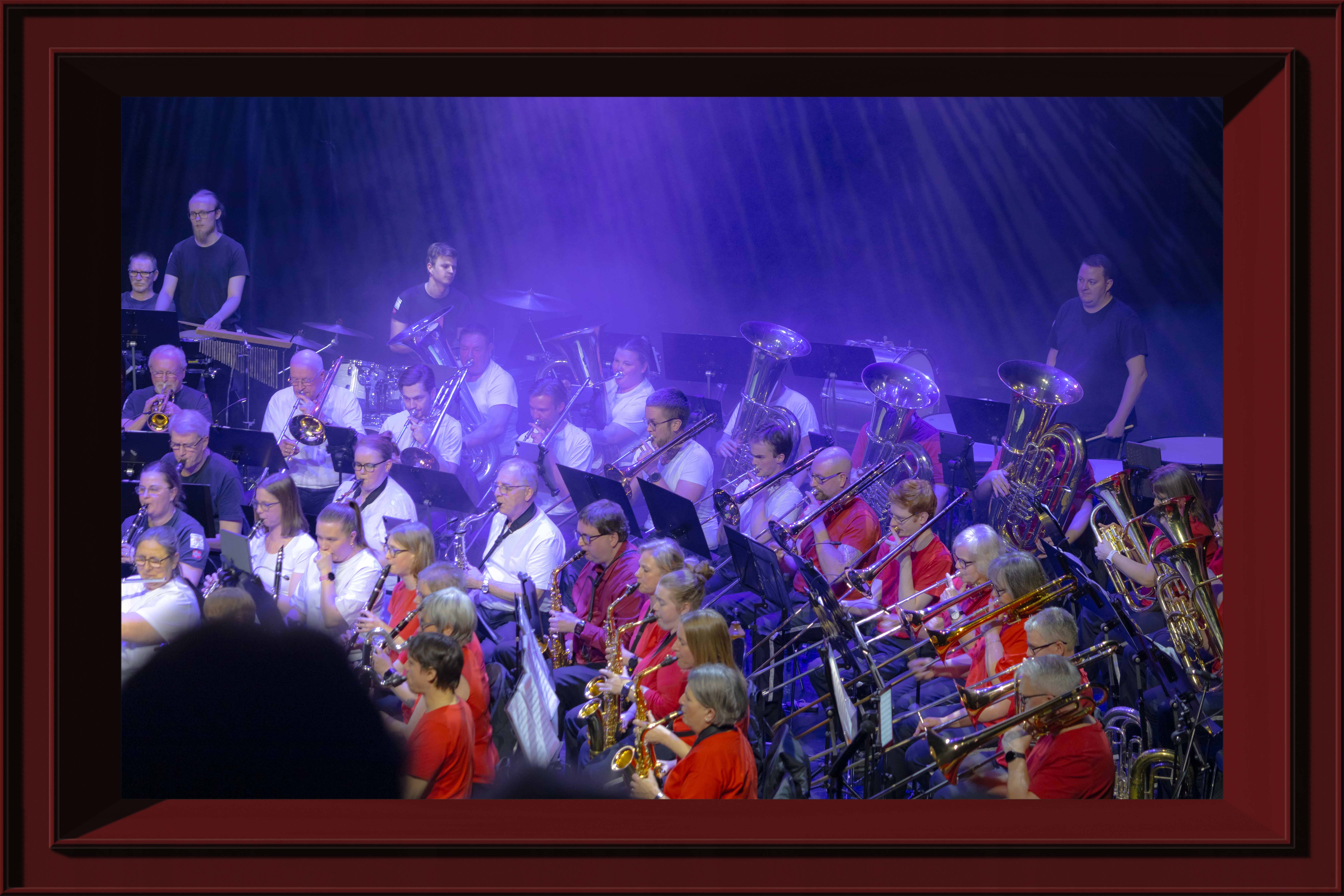 An orchester with vasrious instruments playing music in a concerthall with fog litten up by a purple light, framed in a red frame.